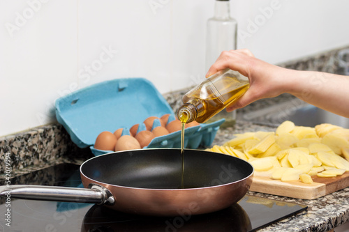 Cropped shot of a woman pouring cooking oil from bottle into frying pan on stove