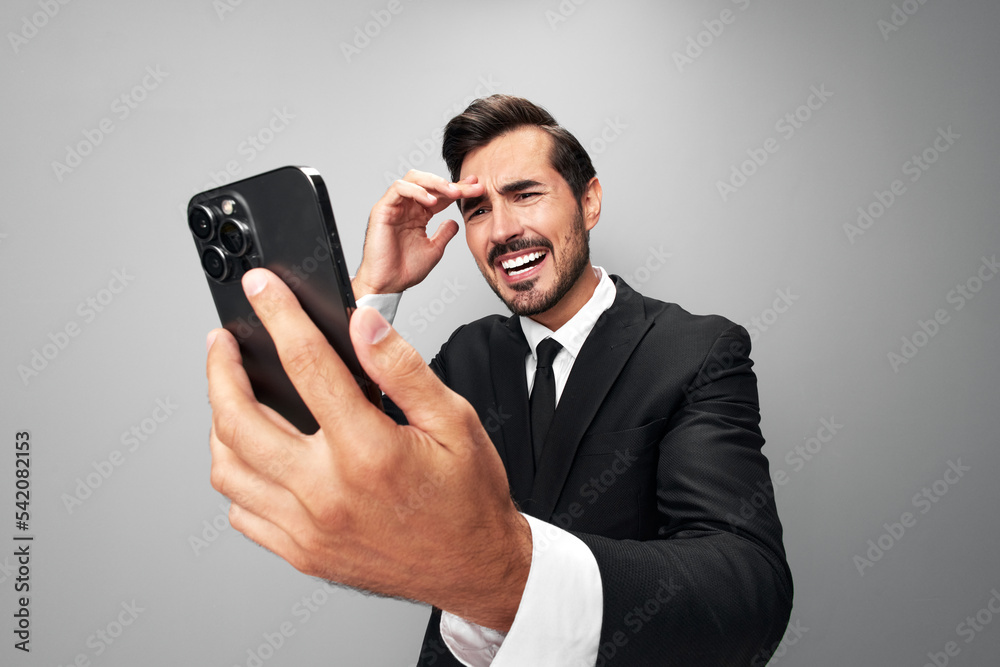 Man businessman holding the phone in his hand looking at him. Headache and anger from failure stress. Close-up wide angle photo gray isolated background Man businessman holding the phone in his hand looking at him. Headache and anger from failure stress. Close-up wide angle photo gray isolated background