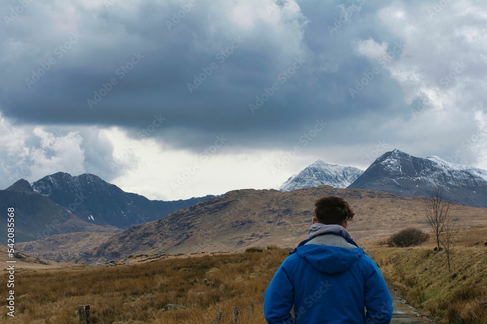 Man standing backwards looking at a majestic mountain range in Wales