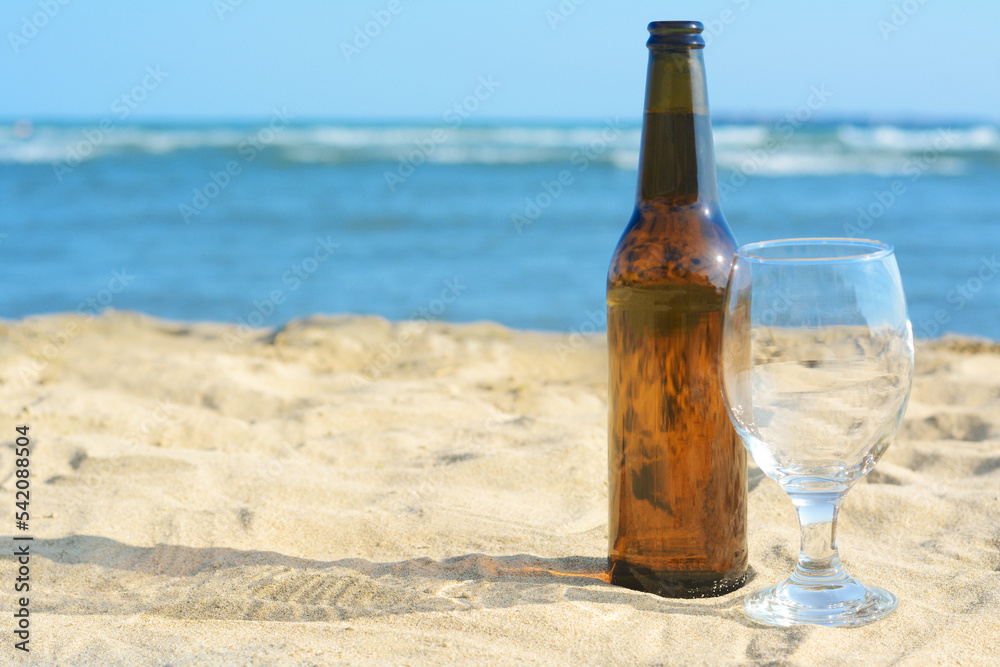 Bottle of beer and glass on sandy beach near sea. Space for text Bottle of beer and glass on sandy beach near sea. Space for text