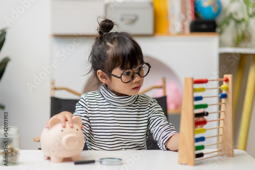 Cute asian child girl putting money into piggy bank to save money for the future