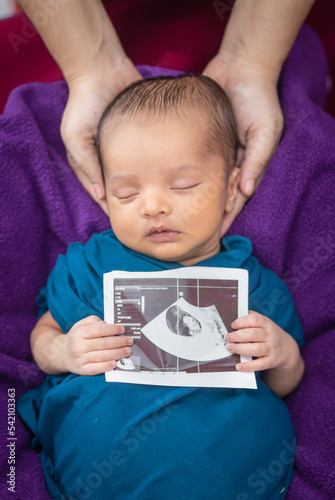 newborn baby holding ultrasound copy in hand and sleeping at mother palm in baby wrap