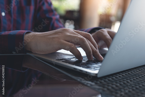 Man hands typing on laptop computer keyboard on table, working at coffee shop, close up