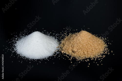 Two piles of sugar on a black background. Comparison of white beet sugar and brown cane sugar.
