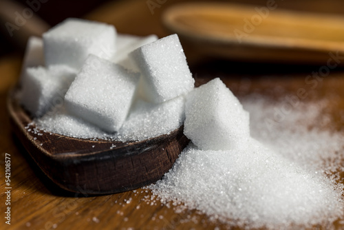 Close up of white sugar cubes on a wooden spoon, on the kitchen table. Preparation of cakes and sweets in the kitchen.