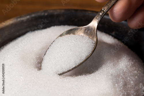 White sugar on a tablespoon, taken from a sugar bowl. Metal spoon with sugar.