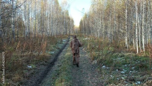 A hunter with a shotgun walks along a forest road in autumn