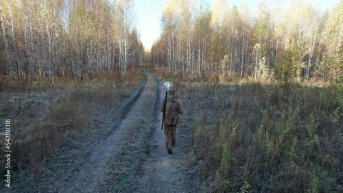 A hunter with a shotgun walks along a forest road in autumn