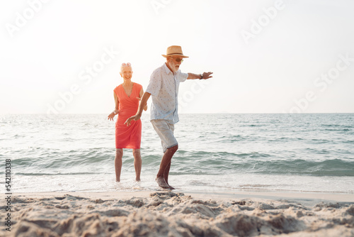 Happy senior couple in love walking and dancing together on the beach having fun in a sunny day, activity after retirement in vacations and summer.