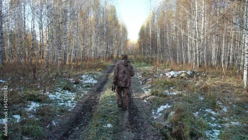 A hunter with a shotgun walks along a forest road in autumn