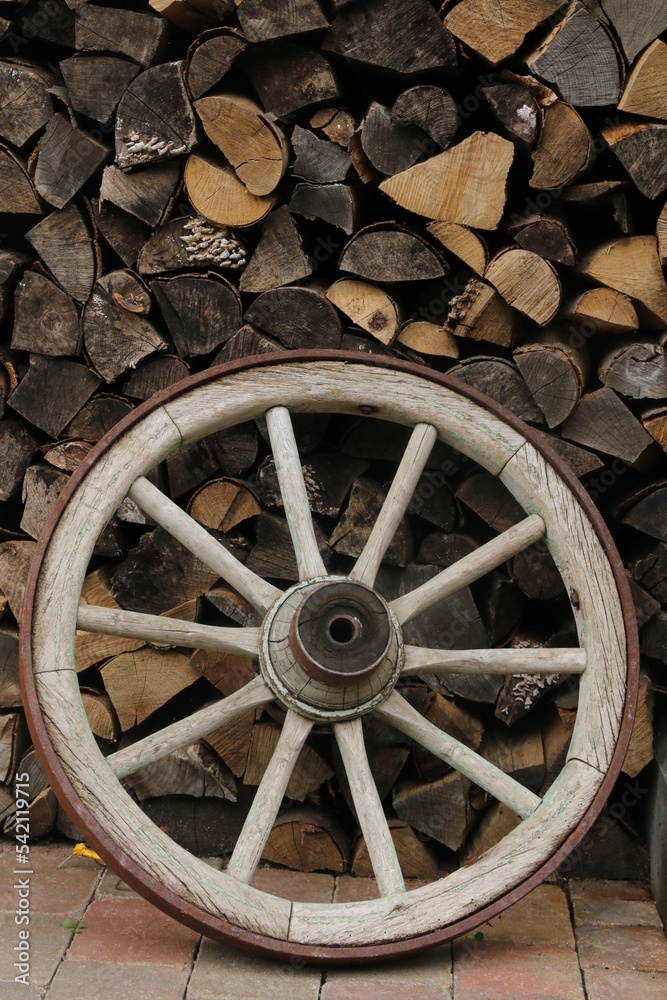 altes Wagenrad vor Brennholzstapel