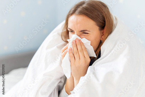 Sick woman sneezing holding tissue paper napkin sitting on couch at home