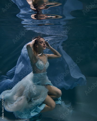 fashionable girl in a beautiful white dress under water in blue light and fluttering fabric in the depths
