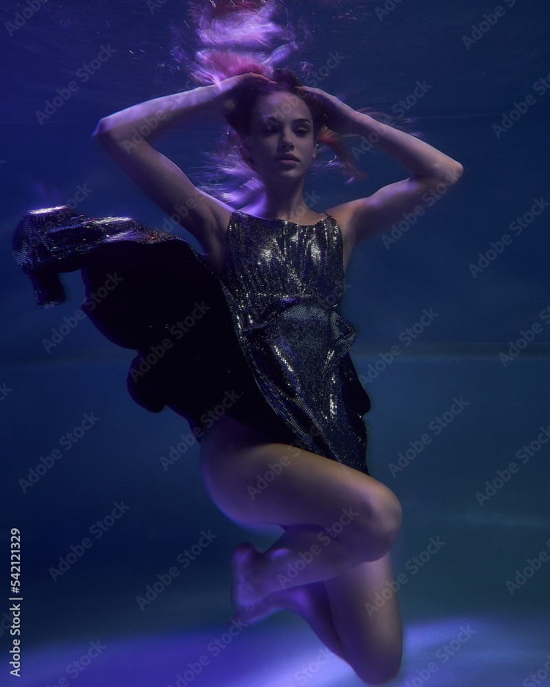 fashionable girl in a beautiful shiny dress underwater in blue light and fluttering fabric in the depths