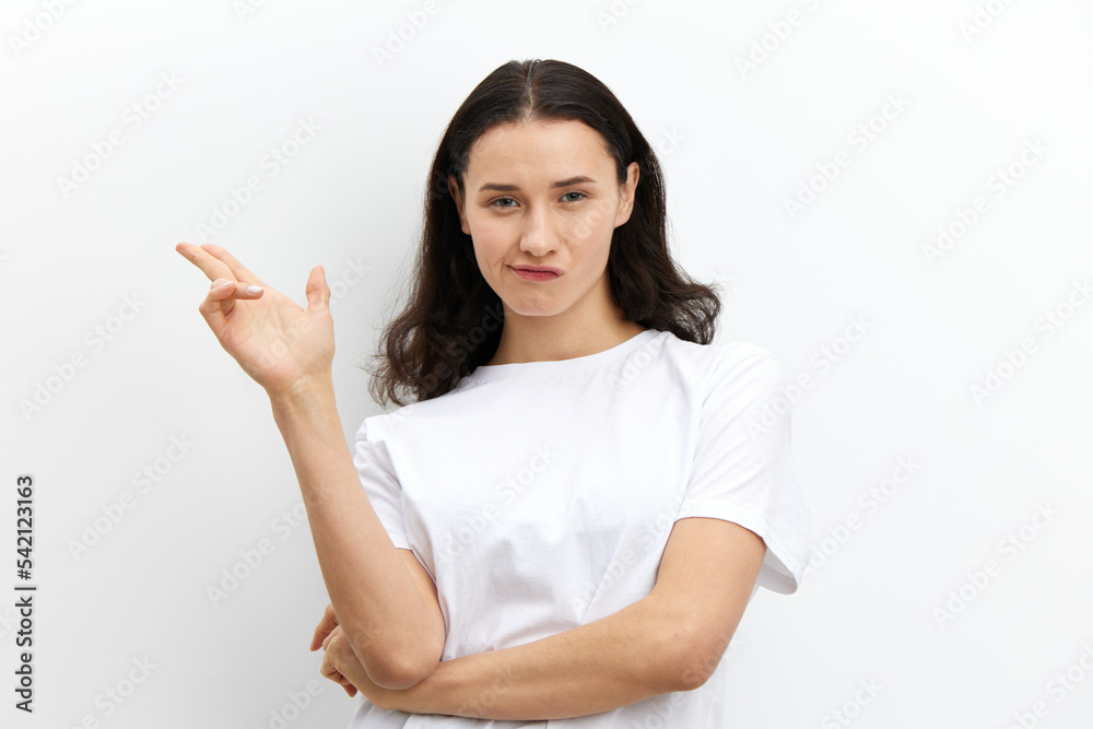 funny, attractive, playful woman shows a pistol sign with her fingers while standing in a white T-shirt on a white background and looking at the camera