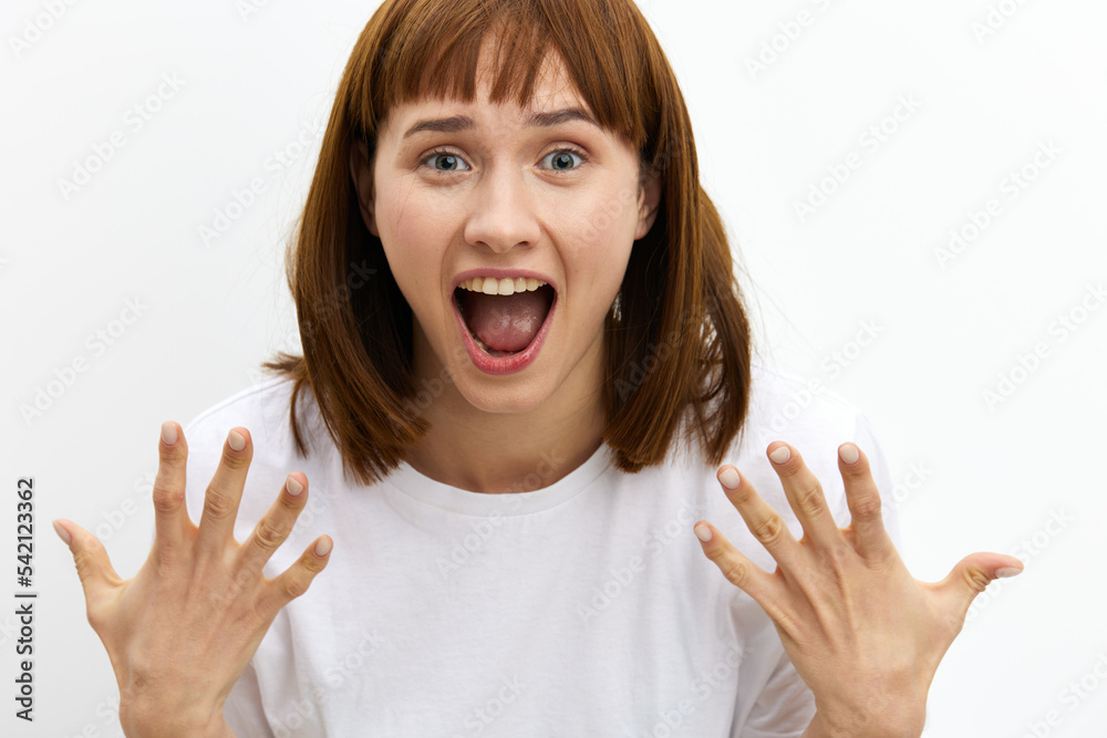 a beautiful, attractive woman stands on a white background in a white T-shirt and screams loudly with delight, actively gesticulating with her hands and eyes wide open a beautiful, attractive woman stands on a white background in a white T-shirt and screams loudly with delight, actively gesticulating with her hands and eyes wide open