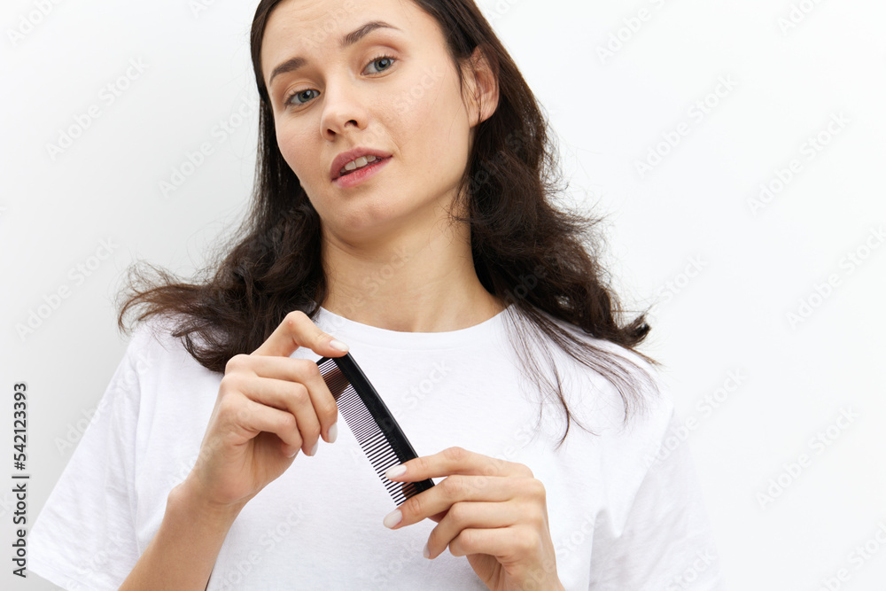 a sweet, pretty woman with long dark hair stands on a white background in a white T-shirt and holds a black comb in her hands, looking pleasantly at the camera a sweet, pretty woman with long dark hair stands on a white background in a white T-shirt and holds a black comb in her hands, looking pleasantly at the camera