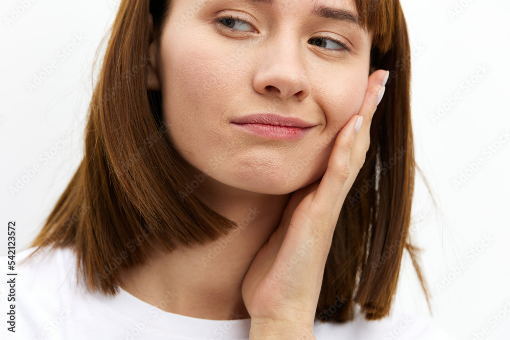 a close horizontal photo of a funny, thoughtful woman in a white T-shirt on a white background holding her hand on her cheek and looking away a close horizontal photo of a funny, thoughtful woman in a white T-shirt on a white background holding her hand on her cheek and looking away