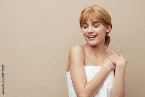 a joyful, admiring woman with perfect skin stands on a beige background, smiling pleasantly, turning her face to the side. Close horizontal photo with empty space