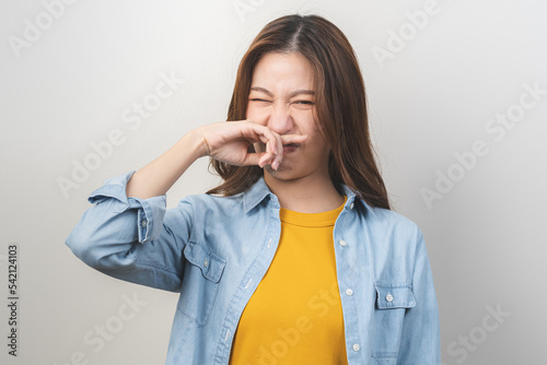 Portrait of pretty brunette hair, disgust smell bad strong asian young woman, girl hand squeezing, covering nose with fingers, expression face disgusting, dislike odor isolated on white background.