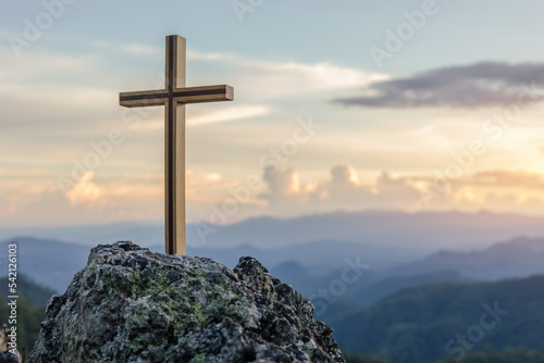 Christian cross on top rock mountain with bright sunbeam on the colorful sky background. Christian background concept