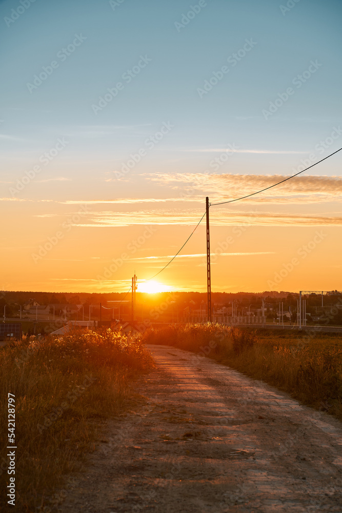 Rural country road at the beautiful summer sunset nature landscape. Empty road and tranquil evening scene with warm sunlight. The dramatic sky above the farm.
