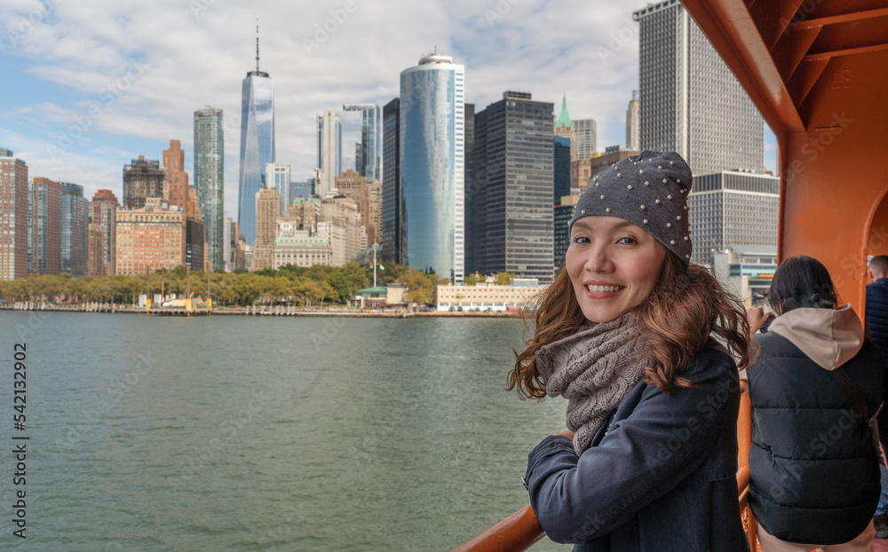  Asian tourist stands on a ferry overlooking the central business building in Manhattan in New York City, USA. The concept of tourists and landmarks