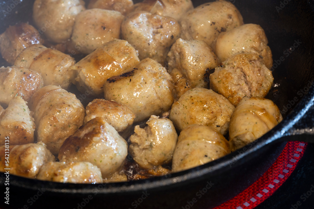 Frying pork sausage meat balls, with olive oil, in a cast iron frying pan, on an electric hob stove Frying pork sausage meat balls, with olive oil, in a cast iron frying pan, on an electric hob stove