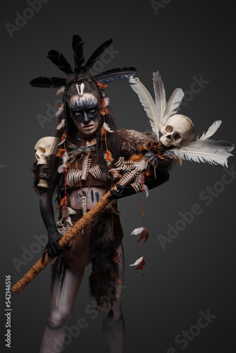 Studio shot of fearful witch woman dressed in plumed attire holding staff. © Fxquadro