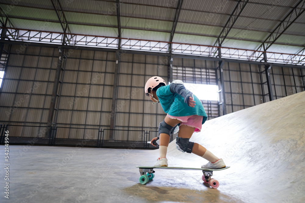 asian child skater or kid girl fun playing skateboard or riding surf skate and get off ramp or down from wave bank to bottom turn surfing in skatepark by extreme sports to wear helmet for body safety