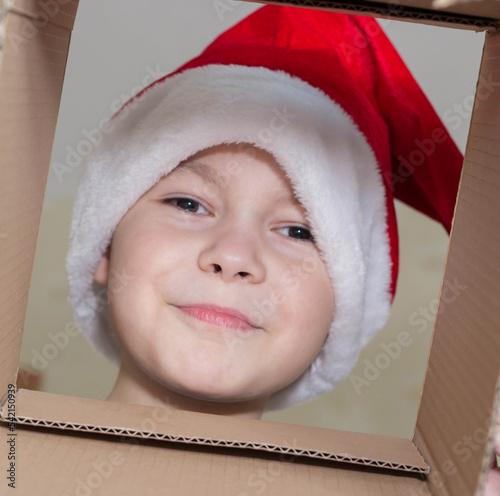 Little Christmas girl in a Santa hat looks into a gift box. Child is happy with a New Year's gift. The background is defocused light. The concept of Christmas and New Year 2022. High quality photo