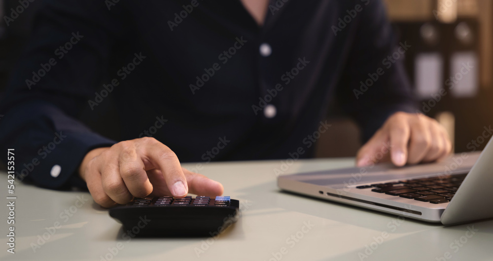 Businessman working with laptop and using a calculator to calculate the tax of static in office. Finance accounting concept. Businessman working with laptop and using a calculator to calculate the tax of static in office. Finance accounting concept.