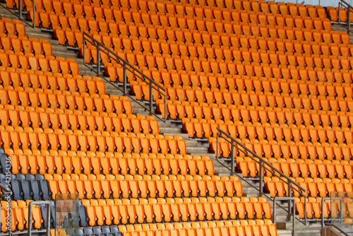 rows of vacant orange fold down seats at a sports stadium
