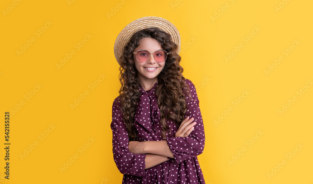 glad kid in straw hat and sunglasses with long brunette curly hair on yellow background