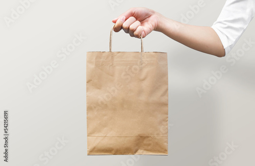 Woman's hand holding an empty brown paper bag. Packaging template mockup. Recycled, eco friendly, and shopping concept