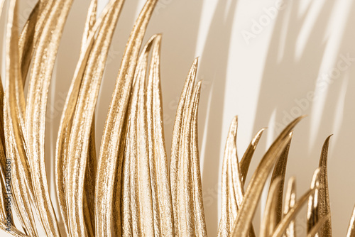 Golden palm leaf close up as styled botanical background  beige monochrome image. Painted metallic golden tropical plant. Creative aesthetic elegant background for spa  wedding  beauty