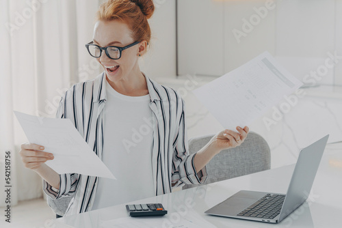 Schilderij op canvas Positive young woman with red hair calculates utility charges engaged in plannin