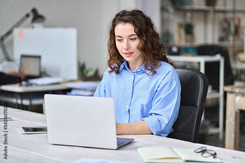 Young business woman company employee sitting at desk working on laptop. Busy female professional worker marketer using computer in corporate modern office managing data technology operations. Young business woman company employee sitting at desk working on laptop. Busy female professional worker marketer using computer in corporate modern office managing data technology operations.