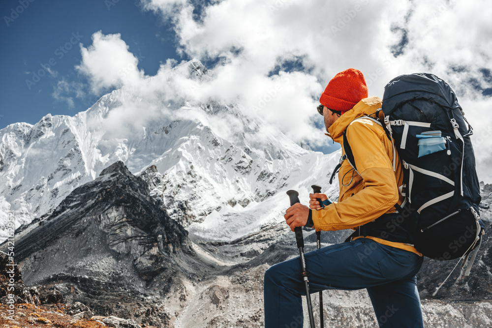 Young tourist walk along high altitude track among snowy and cloudy mountains. Man expeditor with travel backpack going across rocky way