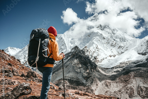 Professional expeditor with trekking sticks and traveling backpack going by mountains tack. Solo tourist hiking across high snowy mountain photo