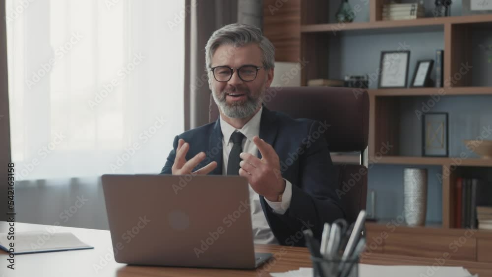 Confident businessman using a laptop talking to a camera making a conference business call in the office. Male professionals communicating by videoconference. Modern room. Close up Confident businessman using a laptop talking to a camera making a conference business call in the office. Male professionals communicating by videoconference. Modern room. Close up
