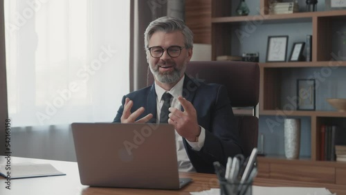 Confident businessman using a laptop talking to a camera making a conference business call in the office. Male professionals communicating by videoconference. Modern room. Close up