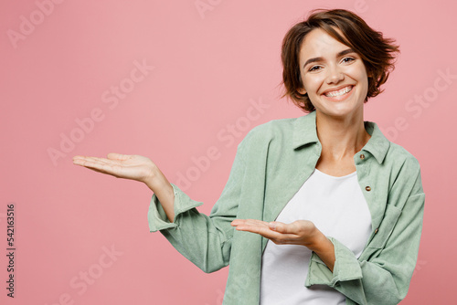 Print op canvas Young smiling cheerful happy cool woman 20s wear green shirt white t-shirt point hands arms aside on workspace area mock up copy space isolated on plain pastel light pink background studio portrait