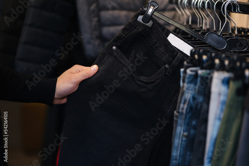 Close up of human hand taking black jeans. Trousers for man