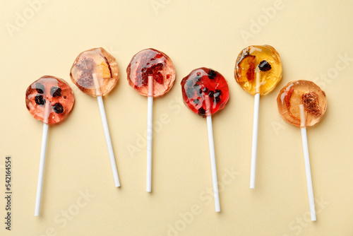 Sweet colorful lollipops with berries on beige background, flat lay