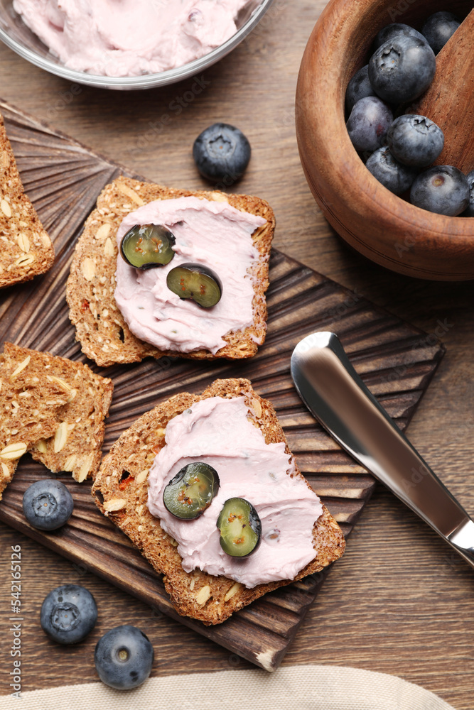 Tasty sandwiches with cream cheese and blueberries on wooden table, flat lay Tasty sandwiches with cream cheese and blueberries on wooden table, flat lay