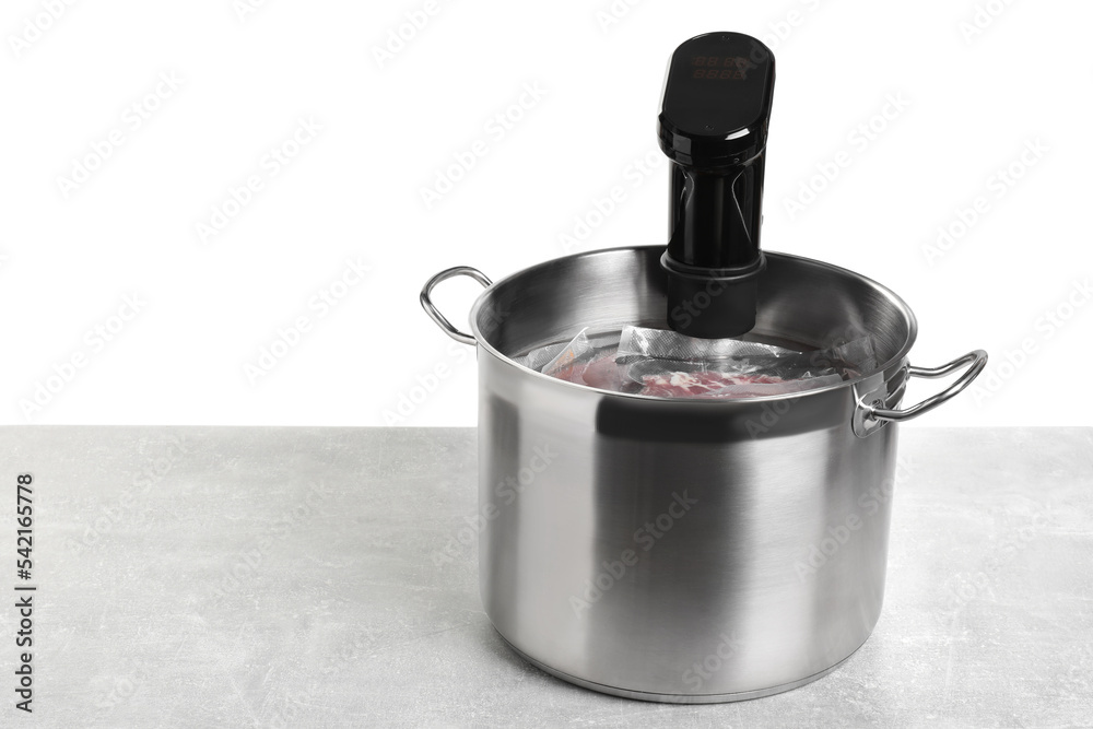 Sous vide cooker and vacuum packed food products in pot on light marble table against white background, space for text. Thermal immersion circulator Sous vide cooker and vacuum packed food products in pot on light marble table against white background, space for text. Thermal immersion circulator