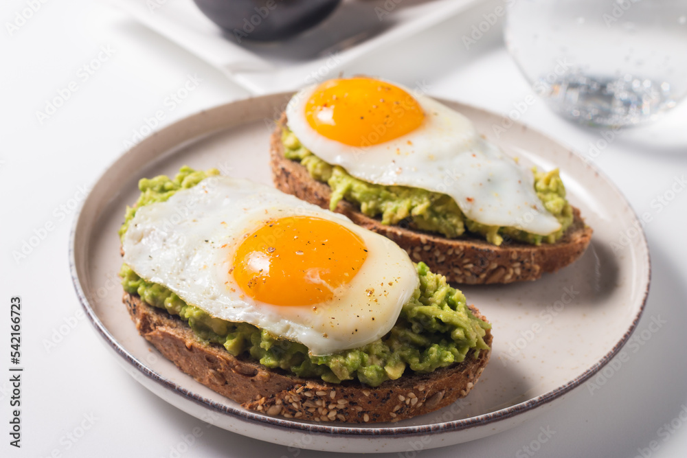 Avocado egg sandwich with a glass of water. Healthy light breakfast concept. Whole grain toasts with mashed avocado and fried eggs Avocado egg sandwich with a glass of water. Healthy light breakfast concept. Whole grain toasts with mashed avocado and fried eggs