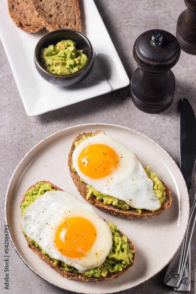 Avocado egg sandwich with a glass of water. Healthy light breakfast concept. Whole grain toasts with mashed avocado and fried eggs Avocado egg sandwich with a glass of water. Healthy light breakfast concept. Whole grain toasts with mashed avocado and fried eggs