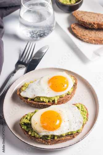 Avocado egg sandwich with a glass of water. Healthy light breakfast concept. Whole grain toasts with mashed avocado and fried eggs